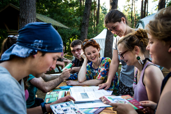 Gruppe junger Menschen guckt gemeinsam Workshopmaterial an. Sie sitzt im Wald.