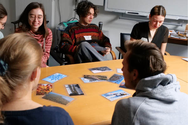 Eine Gruppe junger Menschen sitzt am Tisch mit Postkarten