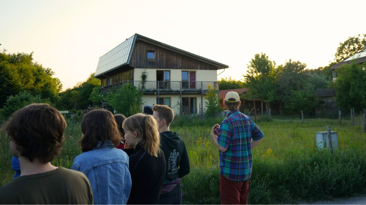 Eine Gruppe junger Menschen von hinten vor einem Seminarhaus im Grünen bei Sonnenuntergang