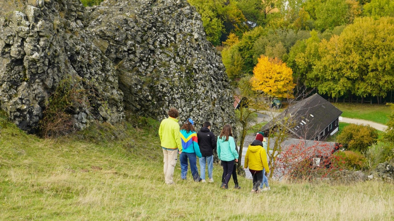 Ein paar junge Menschen mit bunten Jacken laufen einen Hang mit Felsen über einem Wald hinunter